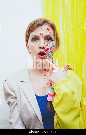 Surprised woman with stickers on face gesturing in front of two tone wall Stock Photo