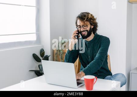 Happy freelancer working on smart phone and talking through smart phone Stock Photo