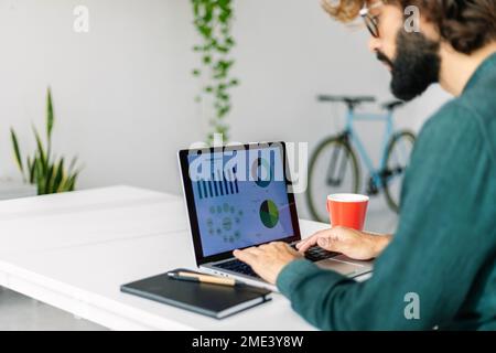 Freelancer analyzing bar graphs and pie chart on laptop in office Stock Photo