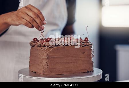 Hand, cake and food with a man chef working in a kitchen while preparing dessert for a party celebration. Cooking, chocolate and cherries with a male Stock Photo