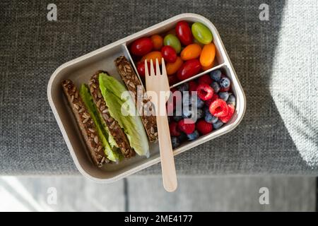 Rye bread, berries and salad with disposable fork in lunch box on sofa Stock Photo