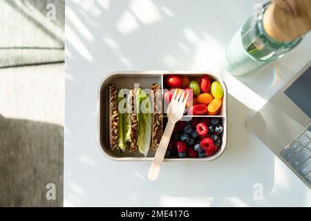 Rye bread, berries and salad with disposable fork in lunch box on table Stock Photo