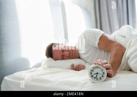 Man holding alarm clock lying on bed in bedroom Stock Photo