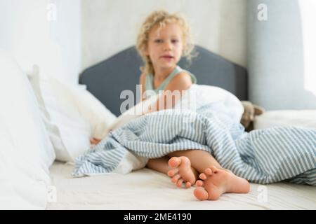Girl with duvet sitting on bed at home Stock Photo