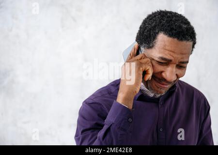 Smiling man talking on mobile phone in front of white wall Stock Photo