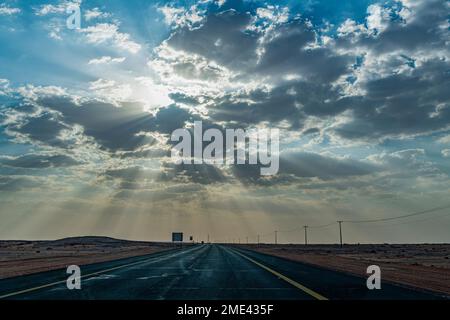 Saudi Arabia, Al-Ula, Setting sun piercing clouds over empty highway Stock Photo