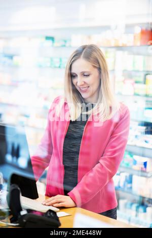 Happy pharmacist working on computer seen through glass Stock Photo