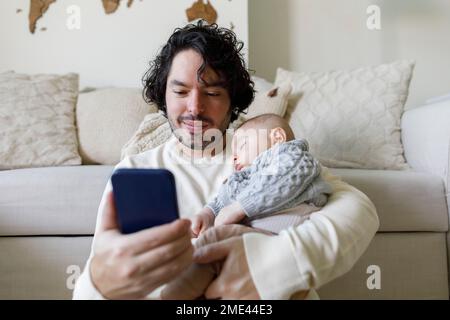 Father using smart phone with baby boy sleeping at home Stock Photo