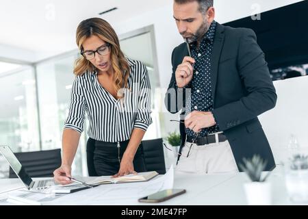 Businesswoman explaining plan to colleague over blueprint Stock Photo