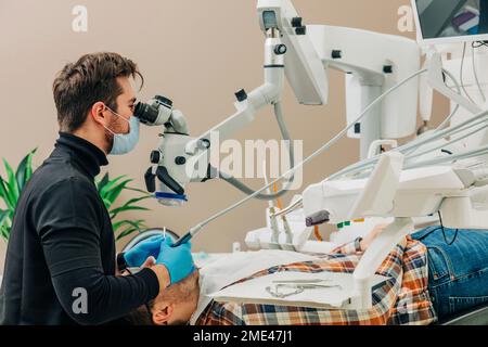 Young dentist examining patient's teeth through microscope in clinic Stock Photo