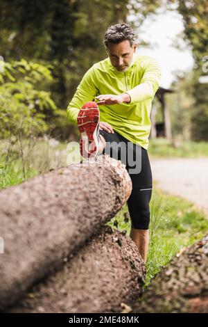 Mature man stretching leg on wooden log Stock Photo
