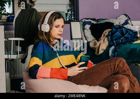 Girl using smart phone listening to music through headphones at home Stock Photo