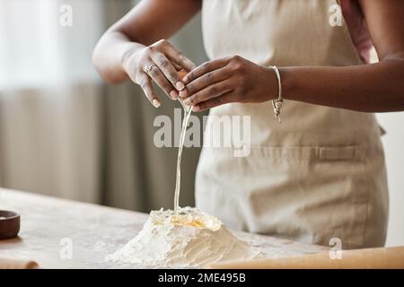 Closeup of black woman baking in kitchen and breaking eggs and mixing with flour while making homemade pastry dough, copy space Stock Photo