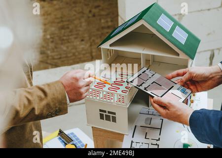 Architects showing colleague underfloor heating of house model using tablet PC at construction site Stock Photo