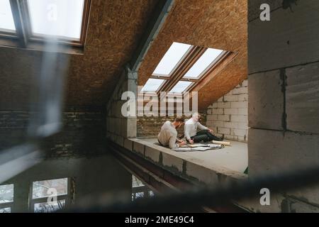 Architects working on blueprint sitting on floor at construction site Stock Photo