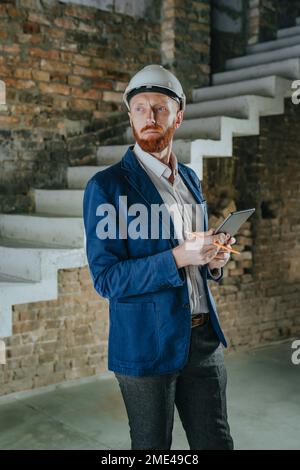 Thoughtful architect standing with tablet PC at under construction site Stock Photo