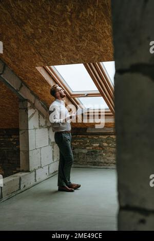 Architect with blueprint looking through window at construction site Stock Photo