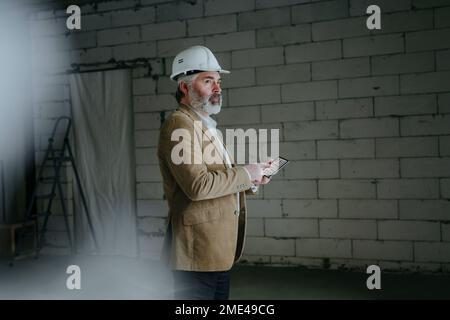 Thoughtful architect standing with tablet PC at construction site Stock Photo