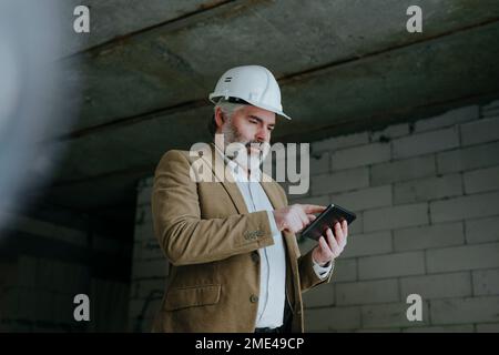 Architect wearing hardhat using tablet PC standing at construction site Stock Photo