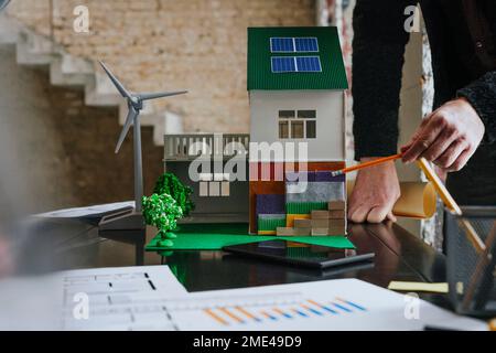 Hands of architect holding compass with house model on desk at construction site Stock Photo