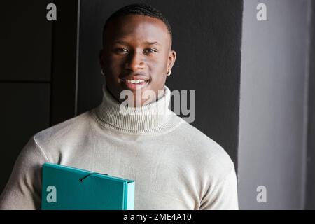 Smiling businessman with file folder in front of wall Stock Photo