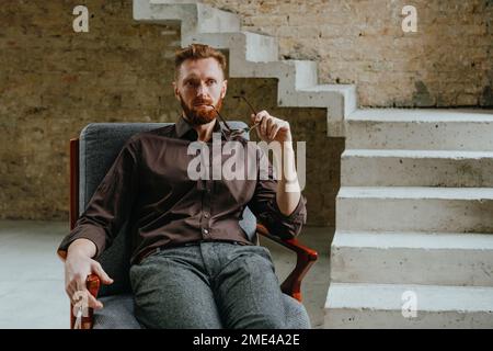Contemplative businessman holding eyeglasses sitting in chair at under construction site Stock Photo