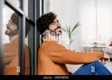 Thoughtful young man leaning on glass door at home Stock Photo