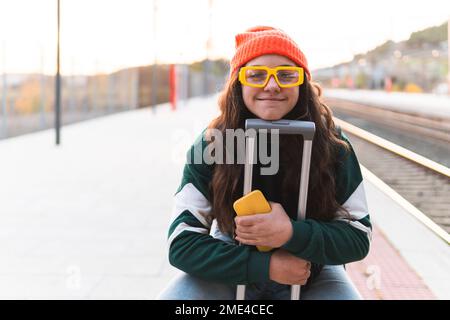 Happy girl wearing knit hat sitting on suitcase Stock Photo