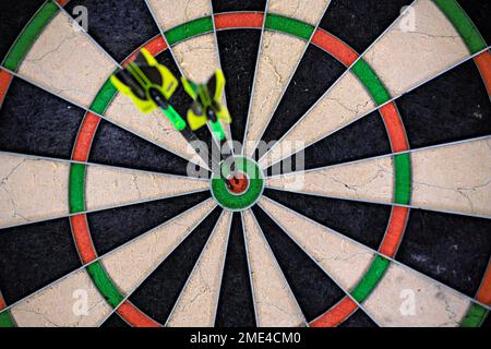 Two black and green darts stuck in the bullseye of a dartboard. Close up of a dartboard. Stock Photo