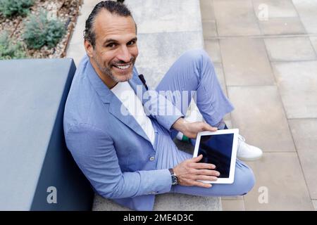 Happy mature businessman with tablet PC sitting on bench Stock Photo