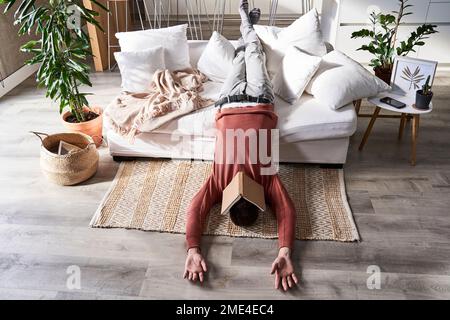 Man with book on face lying upside down at home Stock Photo