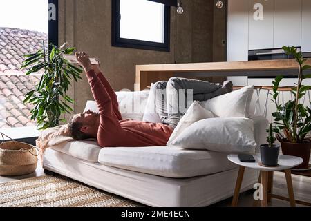 Man lying on sofa reading book at home Stock Photo