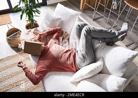 Man lying with book on face in living room Stock Photo