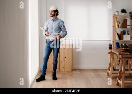 Contemplative smiling architect standing with blueprints in office Stock Photo