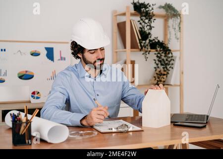 Architect working on house model with blueprints in office Stock Photo