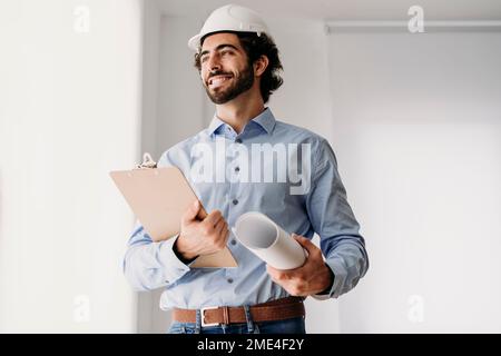 Happy engineer wearing hardhat holding blueprints in office Stock Photo