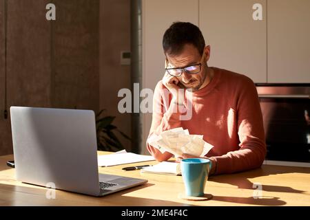 Stressed man examining financial bills sitting at desk Stock Photo
