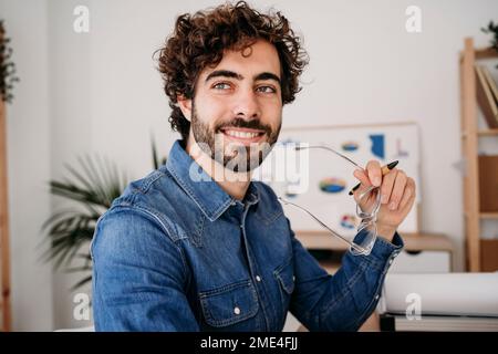 Contemplative young engineer holding eyeglasses in office Stock Photo