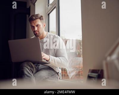 Man by the window at home using laptop Stock Photo