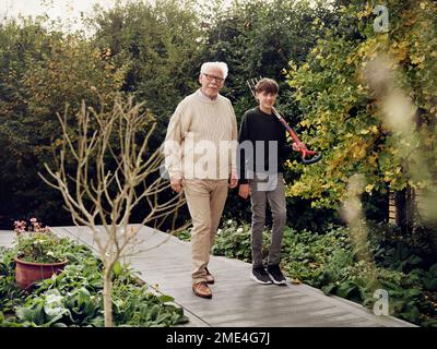 Grandfather and grandson walking in garden boy carrying garden fork Stock Photo