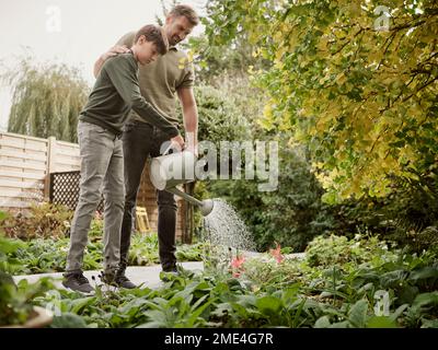 Father and son standing in garden watering plants Stock Photo