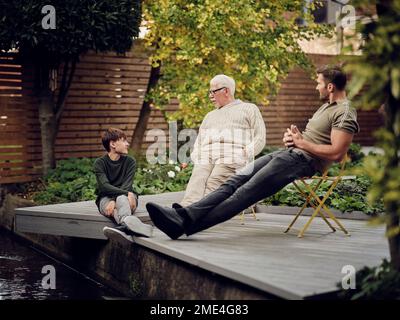 Father, son and grandson sitting at garden pond talking and relaxing Stock Photo