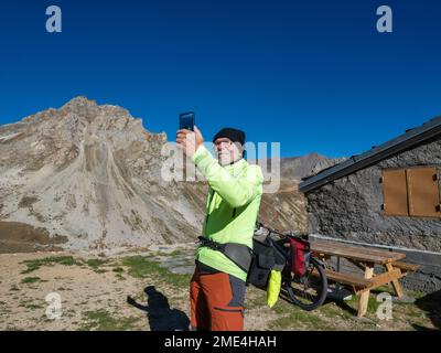 Senior man taking selfie through mobile phone in front of mountain under blue sky at Vanoise National Park, France Stock Photo