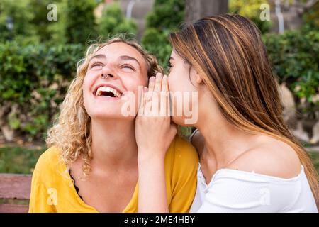 Woman whispering into friend's ear in park Stock Photo