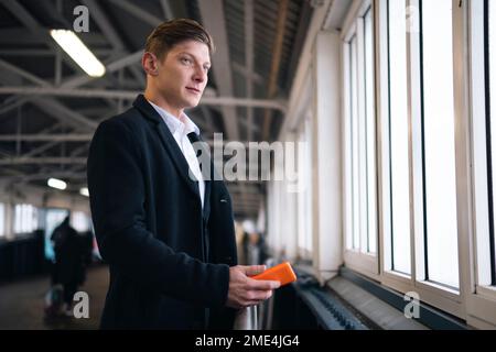Thoughtful young businessman holding smart phone looking out through window Stock Photo