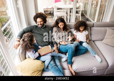 Happy father with mother and daughters reading book on sofa at home Stock Photo