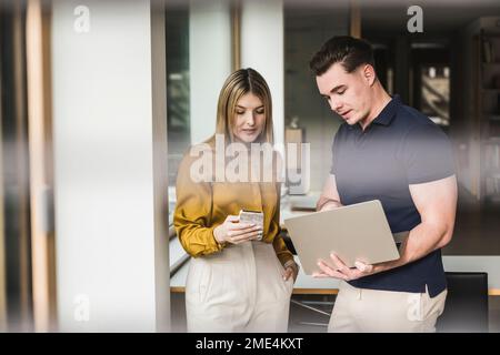 Businessman discussing over laptop with colleague using smart phone in office Stock Photo