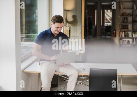 Smiling young businessman working on laptop in office Stock Photo