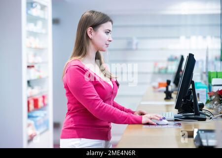Pharmacist working on desktop PC at counter in pharmacy Stock Photo