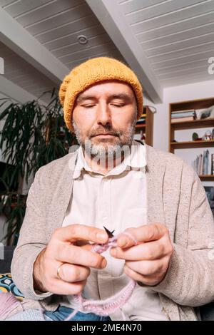Man in warm clothing knitting on couch at home Stock Photo